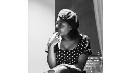 Black and white photo of a woman at a side profile, wearing a beret and a polka dot dress.